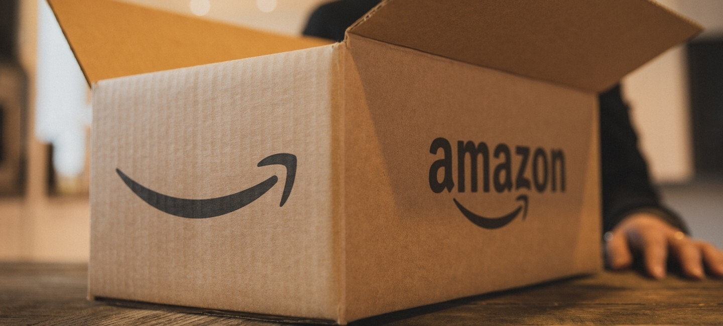 A box with an Amazon smile on it. A woman's hand is visible behind the box. 
