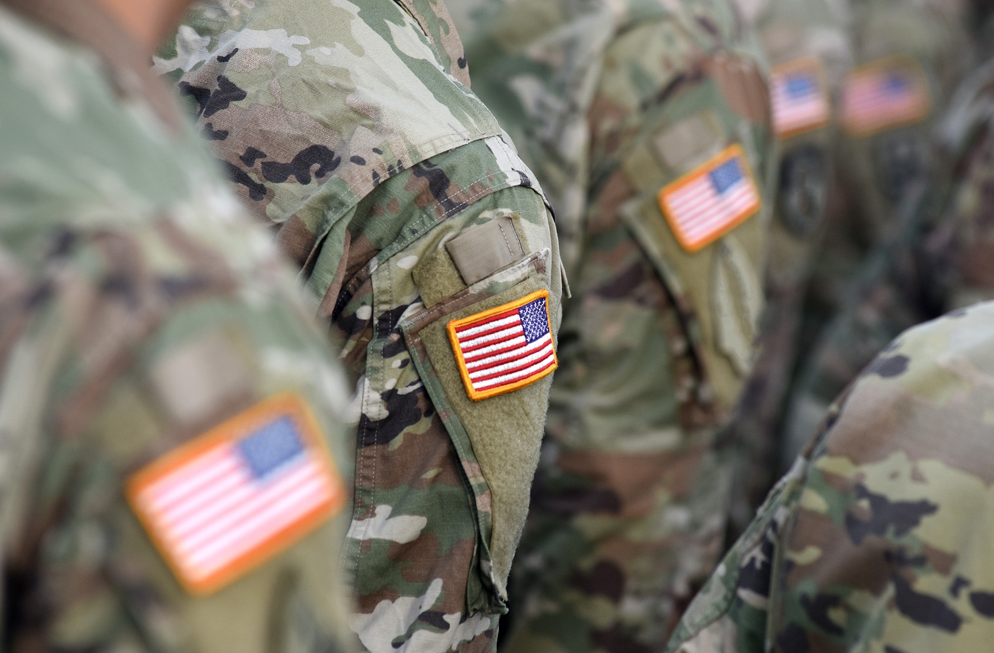 U.S. soldiers stand in close quarters, their shoulders baring a U.S. flag patch. Their faces are obscured.