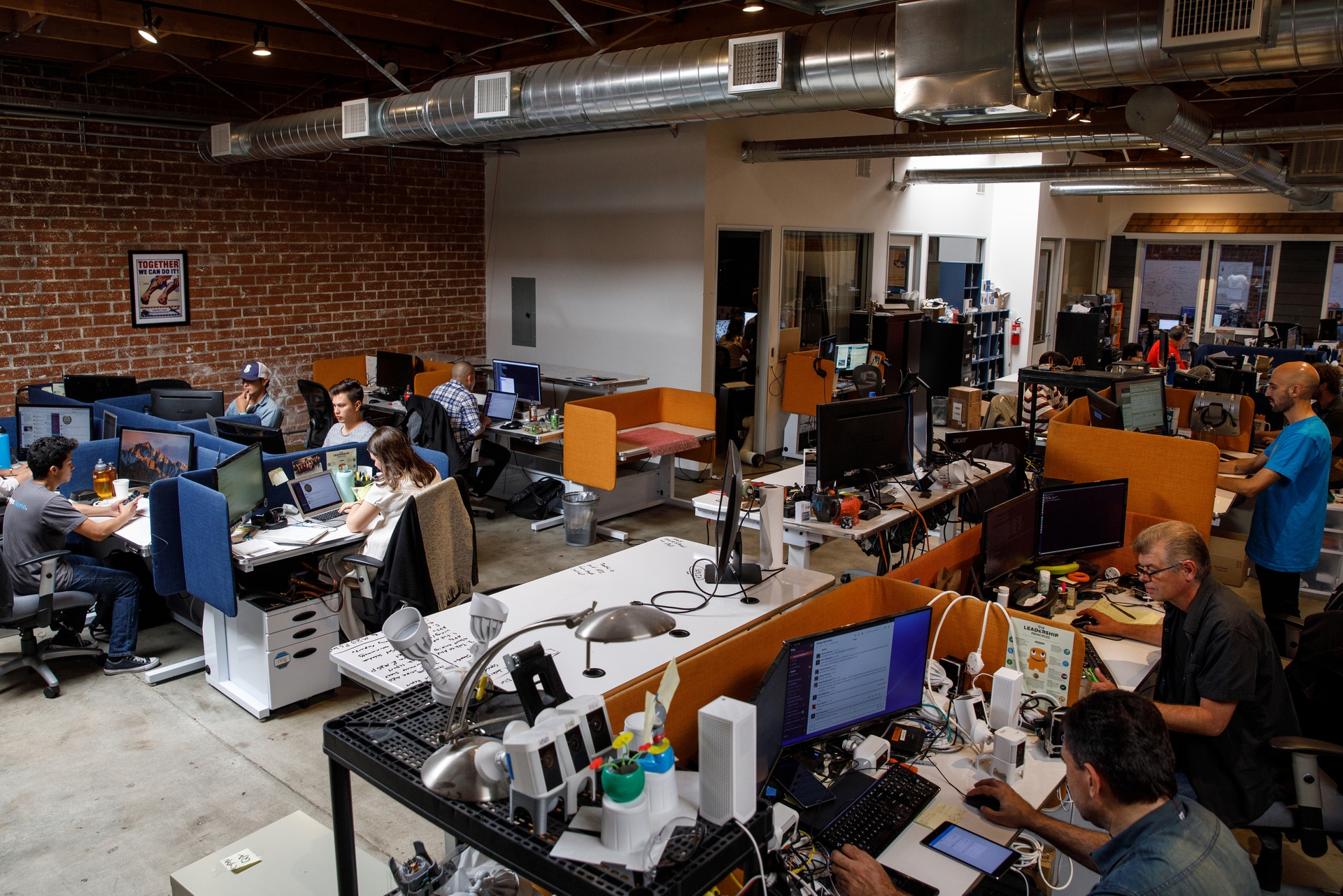 Employees sit at long tables with computers at Ring headquarters in Santa Monica, CA. The walls are brick. 