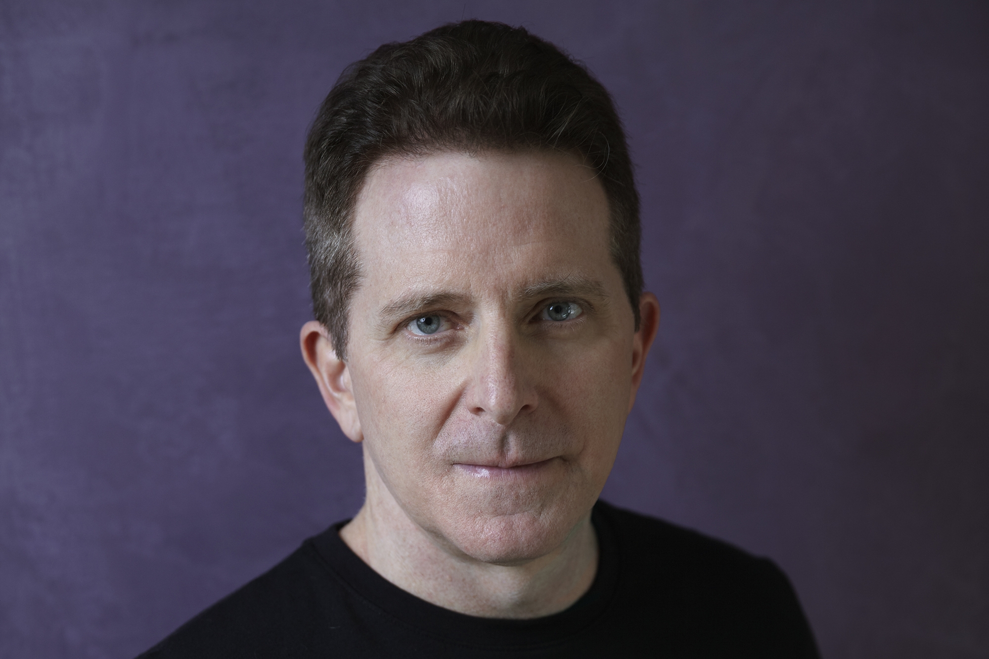 Amazon author Landon J. Napoleon stares into the camera. He has dark hair, blue eyes, and is wearing a black sweater. The background is purple. 