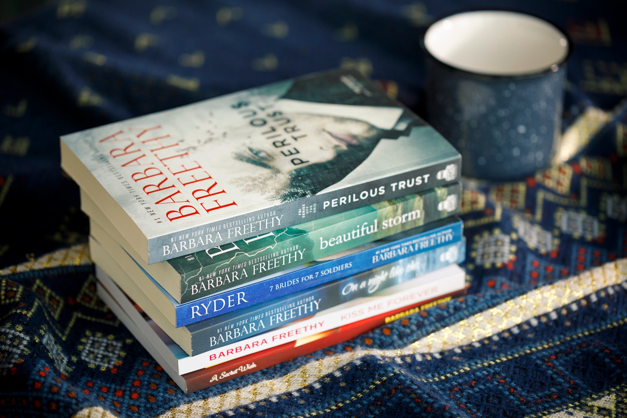 A stack of novels by Amazon author Barbara Freethy sits on a blue tablecloth. A blue coffee cup is in the background. 