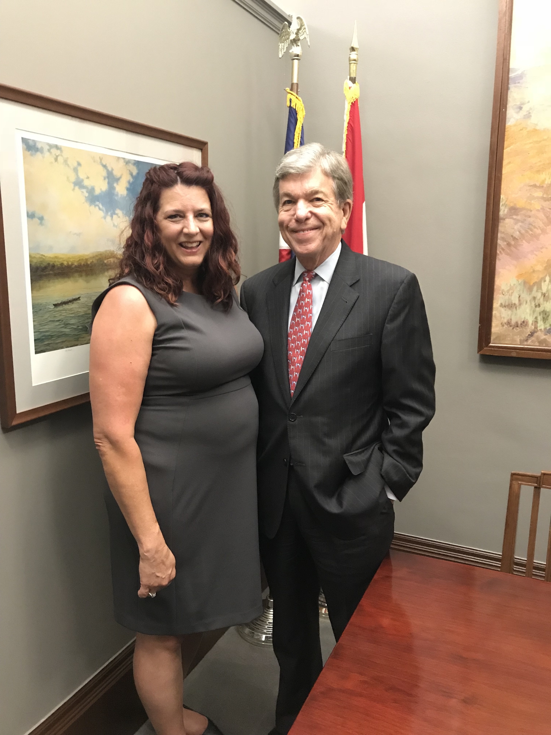 On the left, a female (Kindle Direct Publishing author, Denise Grover Swank) in a dark gray dress stands next to a man (Senator Roy Blunt) wearing a suit. 