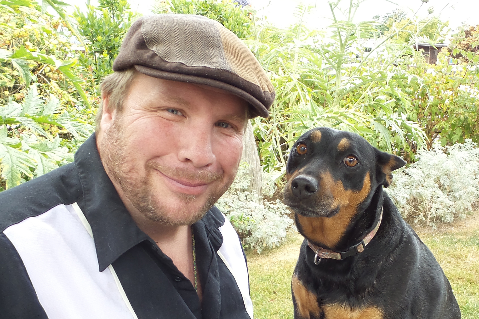An Amazon author in a cap in the woods with his brown and black dog.