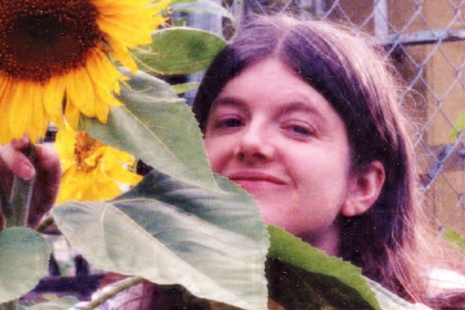 A vintage photo of author Jane Lotter, standing next to sunflower plant.