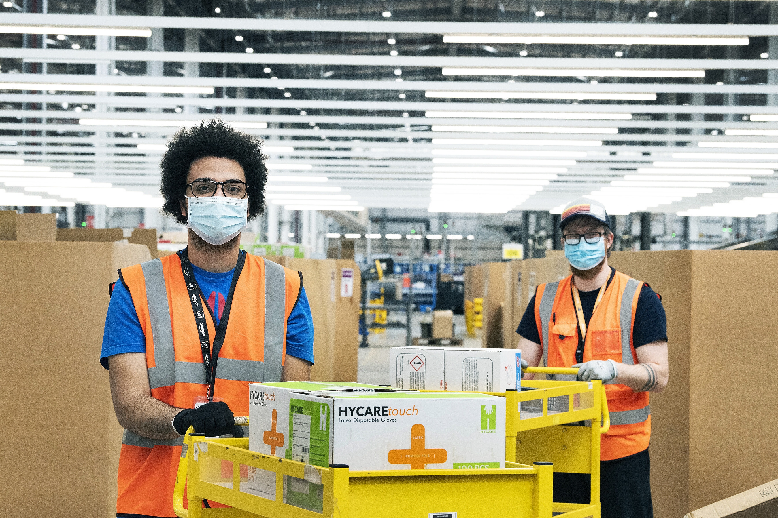 Amazon employees in a fulfilment centre packing medical supplies ready for the government into boxes. They are wearing hi-vis jackets and face masks. 