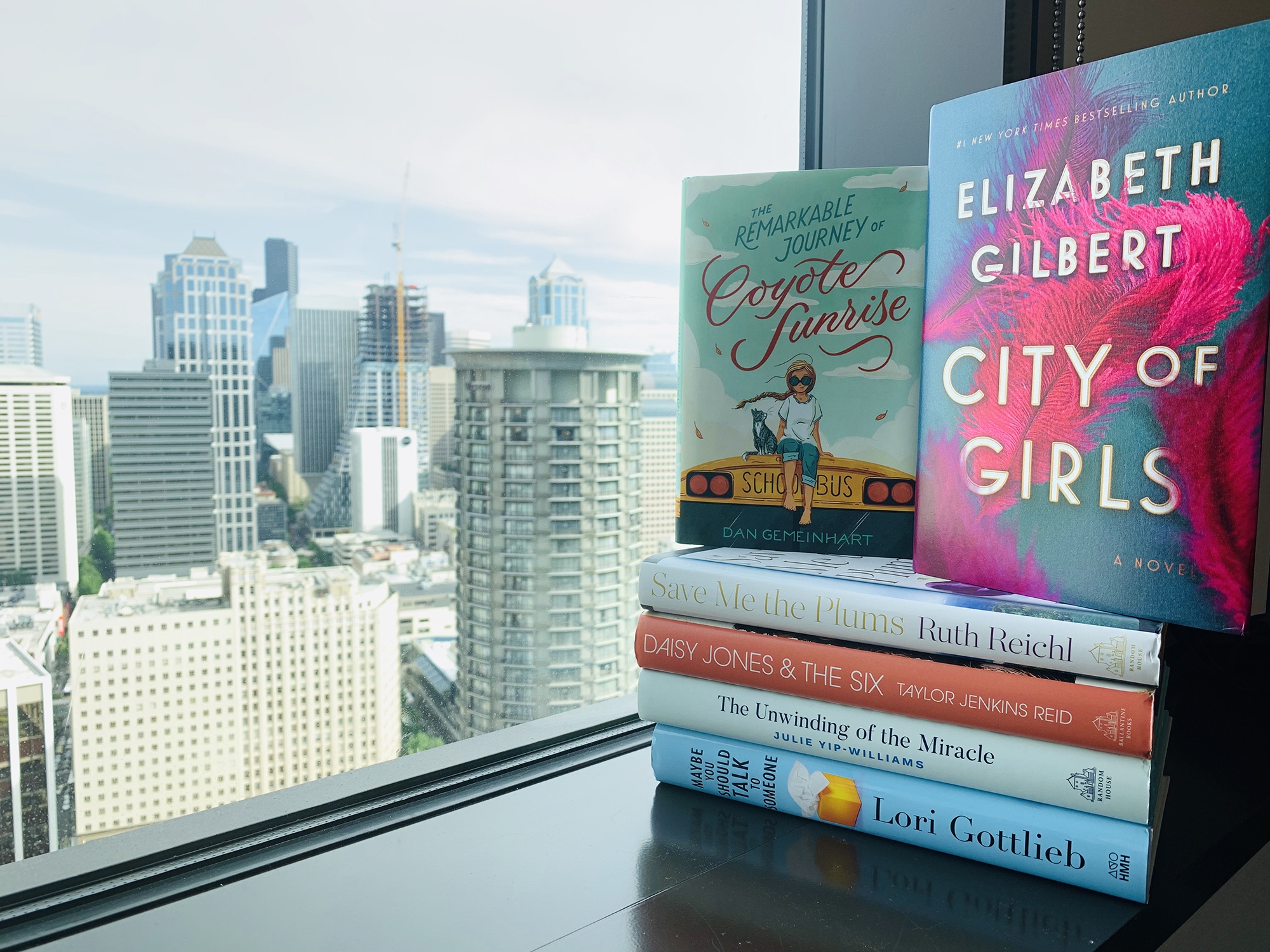 Stack of books in the window overlooking skyscrapers in Seattle. Books are among the "Best books of the year" for 2019.
